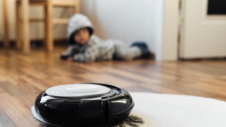 Robotic vacuum cleaner on little white carpet with baby boy on background