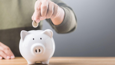 A man drops a coin into a white piggy bank