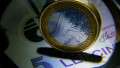 Bucharest, Romania - February 02, 2022: One EURO coin and its equivalent in Romanian lei, a 5 lei banknote, photographed through a magnifying glass. T