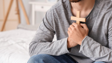 Young man with wooden cross praying in bedroom, closeup