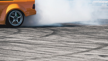 side view of yellow sport car drifting on gray speed tarmac track with smoke coming out of the back tire wheel