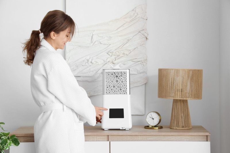 Young woman in bathrobe turning air humidifier on commode at home