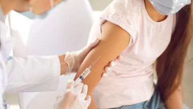 Nurse or doctor giving a flu or Covid 19 shot in the arm to a little girl in a face mask