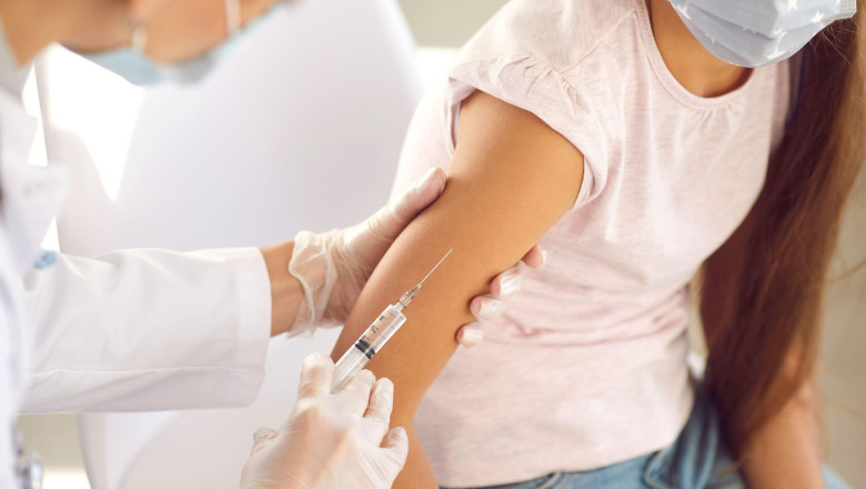 Nurse or doctor giving a flu or Covid 19 shot in the arm to a little girl in a face mask