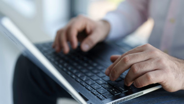 un barbat scrie la laptop
