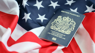 Blue British passport on United States national flag background close up. Tourism and diplomacy concept. Blue British passport on United States