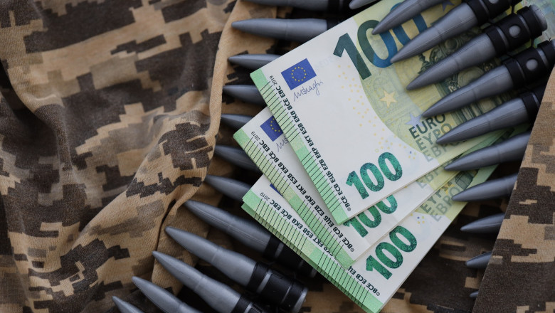 Bundles of euro bills and a machine gun belt on the camouflage uniform of a Ukrainian soldier. Concept of war financing, bribe or donation
