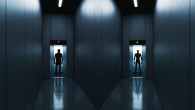 A dark corridor intersection with open elevators—one with a human silhouette entering, the other with a humanoid robot stepping out