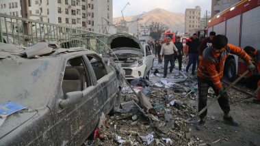 oameni pe strada in teheran, cladire bombardata de israel in fundal