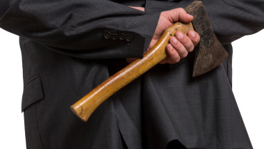 Man in suit hiding an axe behind his back isolated on white background