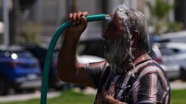 A man washes his head with a garden hose to cool down in a park