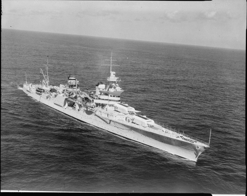 An aerial view of the USS Indianapolis (CA-35), showing its starboard bow while underway. The battleship is moving through the water in a historical naval context.
