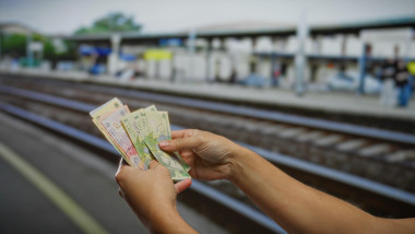 Man holding romanian leu banknotes at a train station, highlighting travel and finance themes in an outdoor setting.