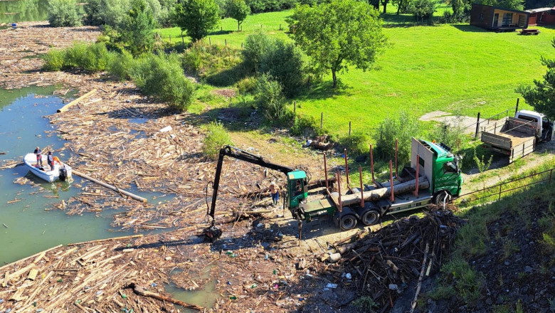 utilaj scoate busteni adusi de viitura din lacul zvorul muntelui