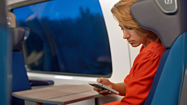 An attractive young woman with red hair and a red dress working online remotely from her phone and travels. Train travel and reading on mobile phone s