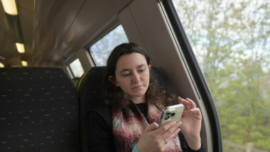 Woman using smartphone while sitting on a train, looking out the window thoughtfully. Germany