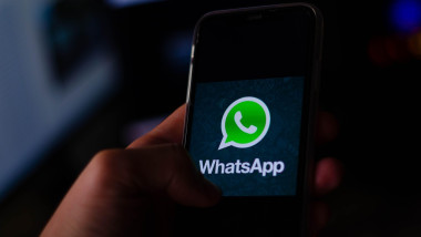 Hands Holding Mobile Smart Phone Device With Whatsapp Company App Logo on Screen and a Notebook with Whatsapp Web