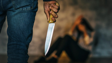 Concept on the topic of domestic violence. A man with a knife in the room threatens the girl