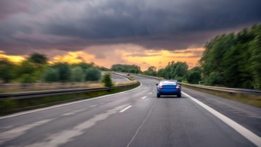 High speed driving. Blue car on highway. Sunset road scene