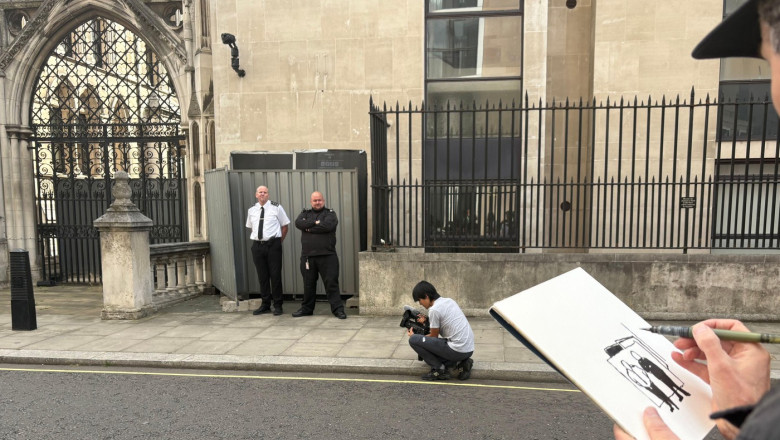 An artist draws the scene, where two security guards are standing next to the wall where a new artwork by artist Banksy has already been covered up at the Royal Courts of Justice in London. The artwork shows a judge attacking a protester with a gavel is o