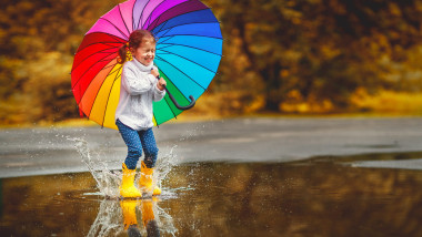fetiță cu umbrelă sărind în baltă și peisaj de toamnă