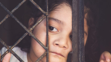 COVID-19 coronavirus concept, little girl in looking through window at home. Sad kid during quarantine due to COVID.