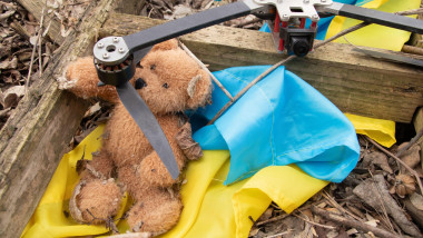 A downed Russian FPV drone lies amidst the ruins of a destroyed house, alongside a child's teddy bear and a Ukrainian flag in Ukraine