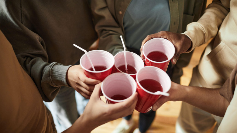 Close-up of young people toasting with plastic cups with alcohol drinks at a party