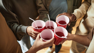 Close-up of young people toasting with plastic cups with alcohol drinks at a party