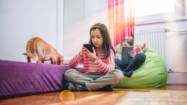 Two girls with small yellow dog sitting in the kids room and using smart phone