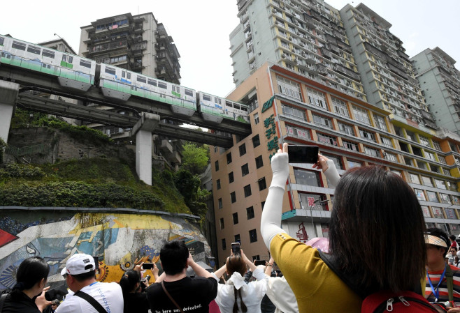Chongqing,China.15th April 2025. Tourists take photos as a light rail train runs through an entire residential building at Liziba Station on April 15, 2025 in Chongqing, China. Located in a 19-storey residential structure, Liziba Station takes the lead in