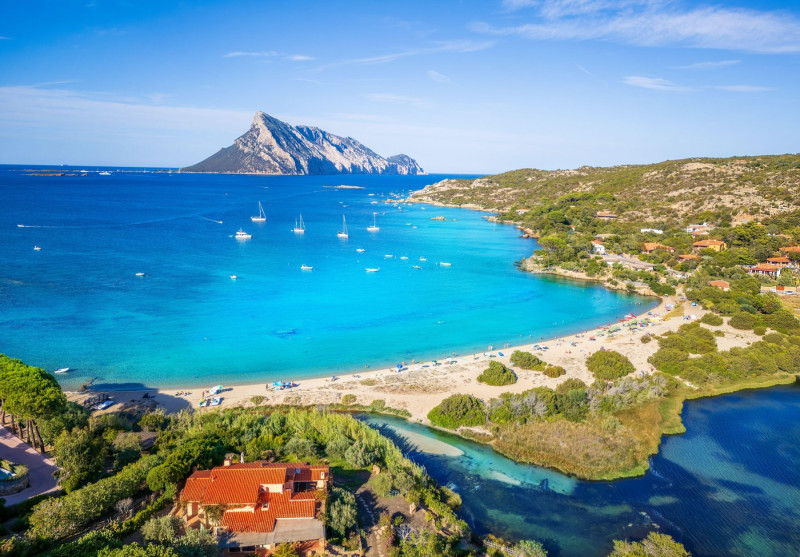 Aerial view of Cala Girgolu beach in Sardinia, Italy with Tavolara Island, turquoise water, sailing boats, nature, and Mediterranean landscape