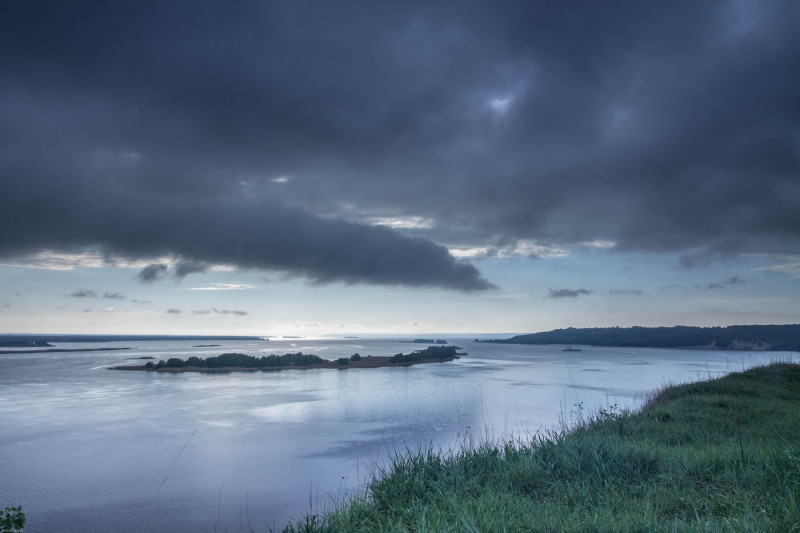 Very cloudy weather. Black clouds over the river. The edge of the river bank.