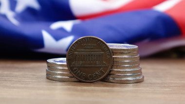 A 1 cent American dollar coin lies on the American flag. The currency is one cent over the flag of the United States