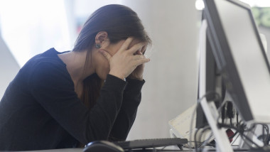 Side view of woman sitting at computer head in hands
