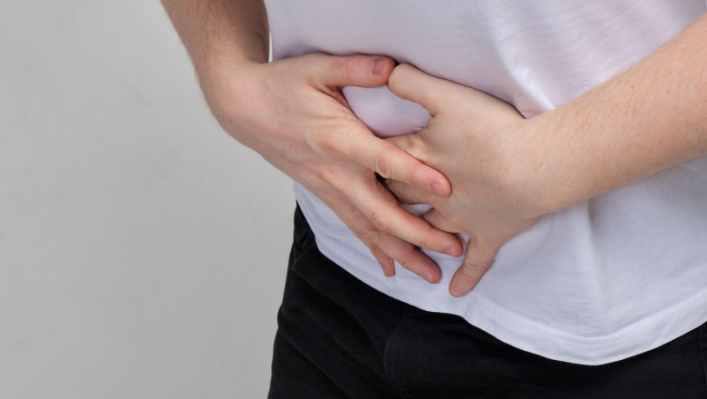 A man in a white T-shirt clutched at his stomach in pain. Food poisoning concept. Close up.