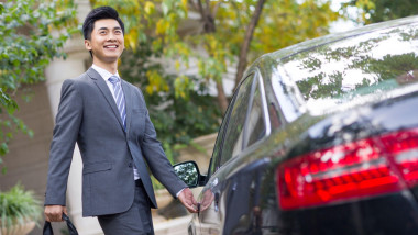 Chinese businessman opening a car door in a garage setting. Smartly dressed with a briefcase, he signals commuting and urban lifestyle. Ideal for mobility, executive travel, and daily life imagery in China.