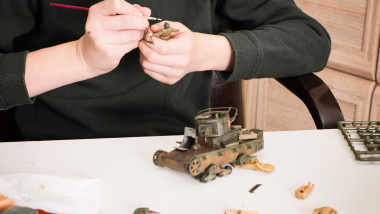 Teen boy assembling painting plastic models of soldiers and tank