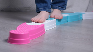 Girl go barefoot on plastic walkway in room. Foot massage. Health and sports, activity. Development of large motor skills. Balance and coordination.