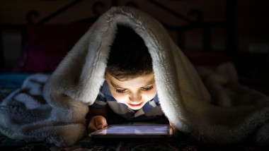 Little child using a tablet covered with a blanket
