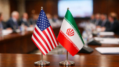 Two small national flags of the United States and Russia placed on a conference table, with a blurred background of an important international meeting