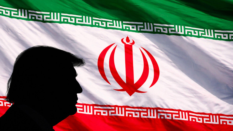 Silhouette profile of former U.S. President Donald Trump positioned on the left against a full-frame, waving Iranian flag, representing geopolitics, i