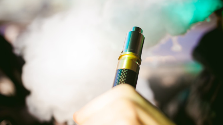 young vaper man with beard vaping mechanical mod. Guy smokes an electronic cigarette by blowing a smoke vapor. Holds in hand on colorful background