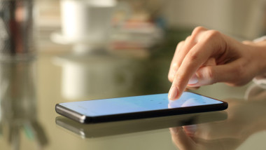 Close up of woman hands entering numbers on a lightened smart phone screen keyboard on a desk at home