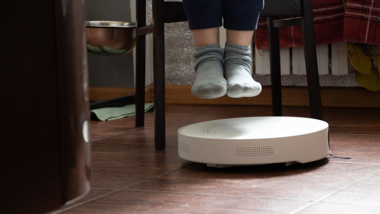 Female legs and a robot vacuum cleaner on the floor doing cleaning in the apartment, cleaning the house