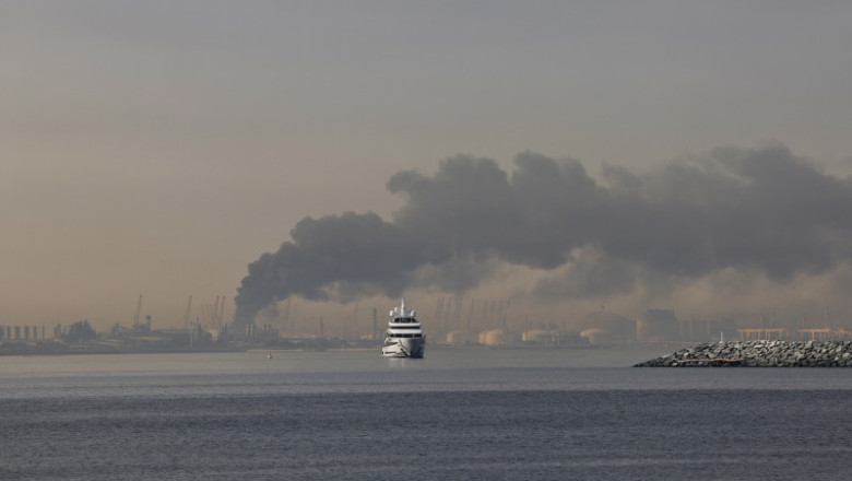 Un iaht navighează pe lângă un nor de fum care se ridică din portul Jebel Ali, în urma unui atac iranian raportat în Dubai, la 1 martie 2026