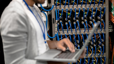 Side view portrait of young man holding laptop against background of blade servers of supercomputer