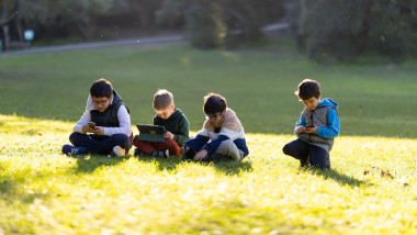 Young boys engaging with digital devices on green grass