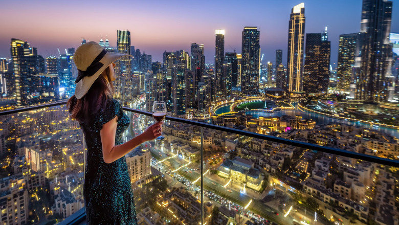 A beautiful woman in a evening dress enjoys the panoramic view over the illuminated skyline of Downtown Dubai, UAE, with a drink in her hand