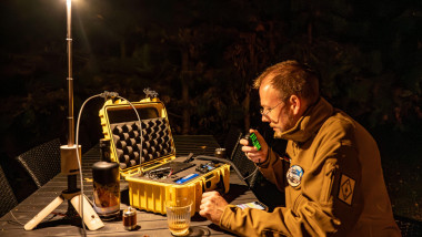 Amateur radio operator in the forest at night, sitting at a table with a portable HF Go-Box setup, communicating off-grid during an outdoor ham radio